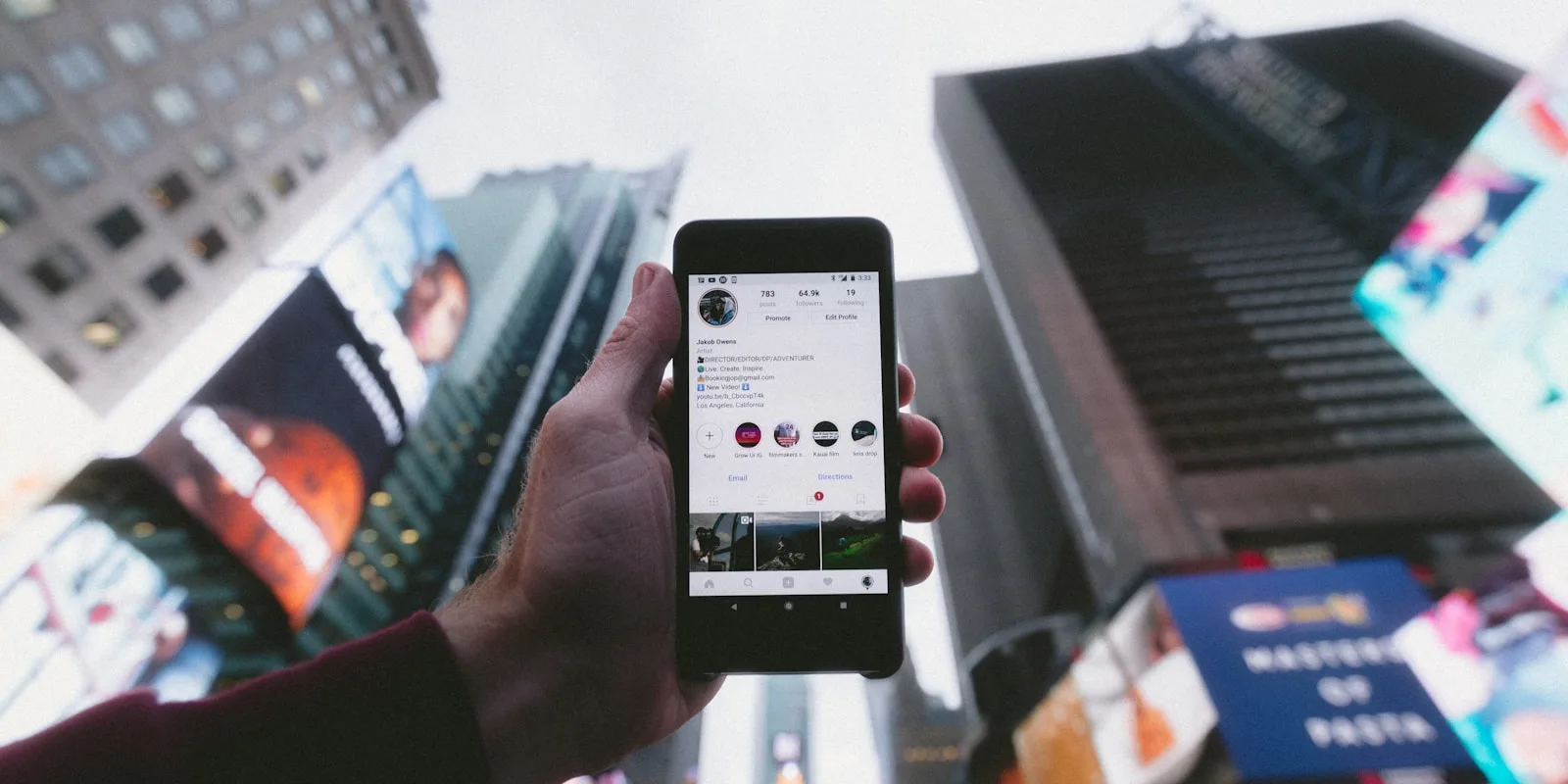 Smartphone showing a social media profile against city billboards