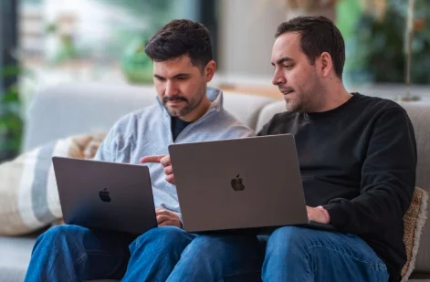 Heiko Guksch und Marcel Hühn nebeneinander auf einem Sofa, jeder mit Laptop